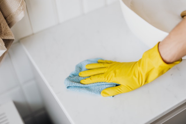hand in yellow rubber glove using blue cloth to wipe a surface